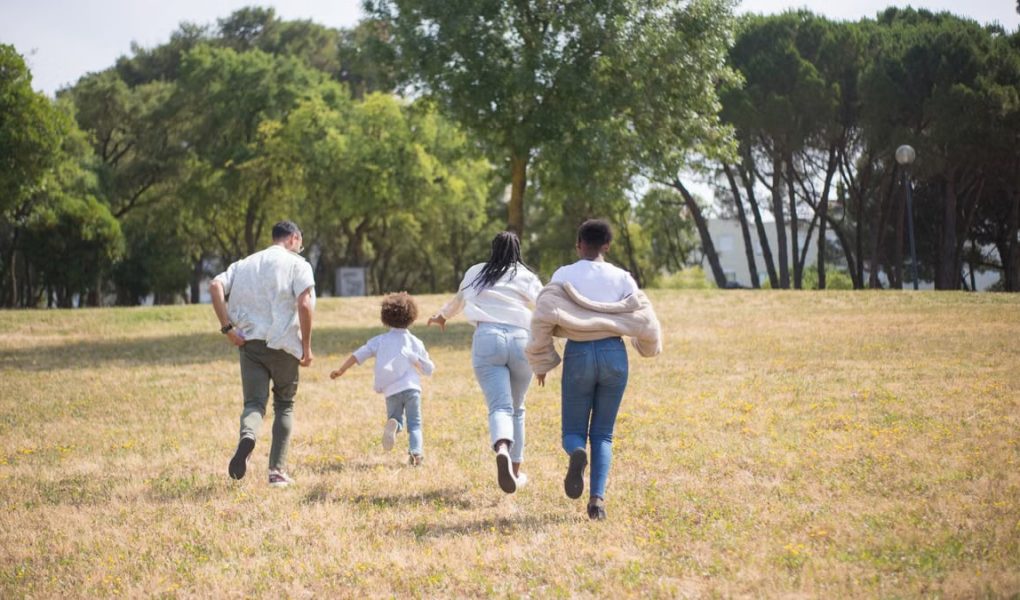 Cheerful family walking together in a sunny park surrounded by trees.