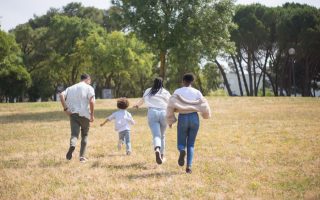 Cheerful family walking together in a sunny park surrounded by trees.