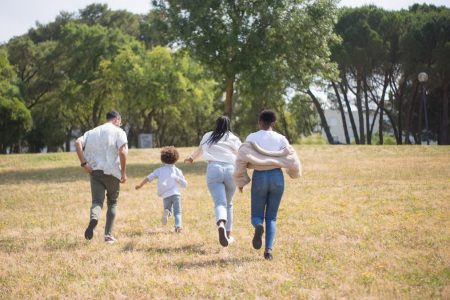 Cheerful family walking together in a sunny park surrounded by trees.