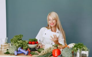 Woman using a tablet surrounded by fresh vegetables at a table, showcasing healthy lifestyle and technology.