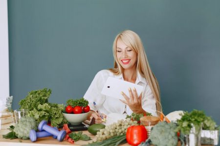 Woman using a tablet surrounded by fresh vegetables at a table, showcasing healthy lifestyle and technology.