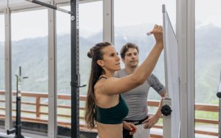 Female fitness coach writes on whiteboard as a male athlete watches in a gym.