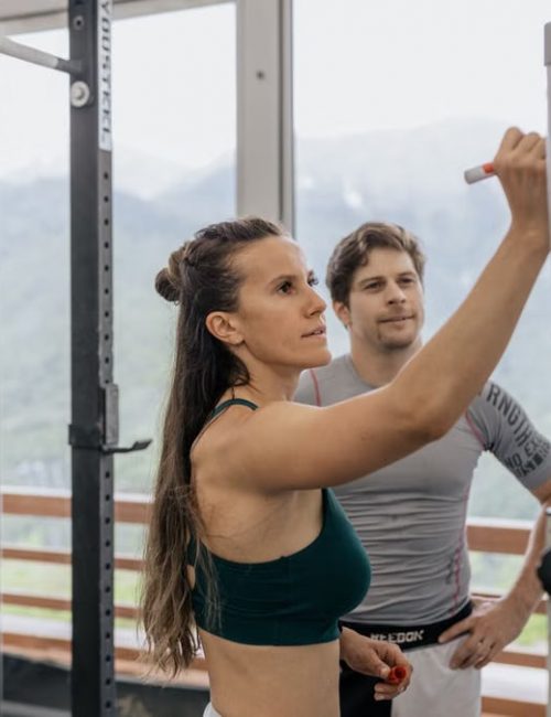 Female fitness coach writes on whiteboard as a male athlete watches in a gym.